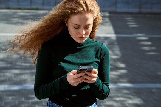 Woman Looks at Phone While Walking on City Street