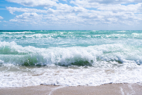 Turquoise waves meet sky under fluffy clouds
