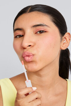 Woman dressed in yellow applying pink lip gloss