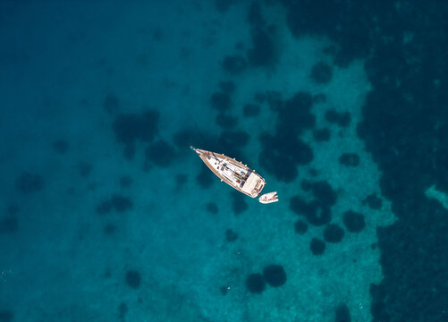Yacht in the sea with reefs bottom, top down drone shot 