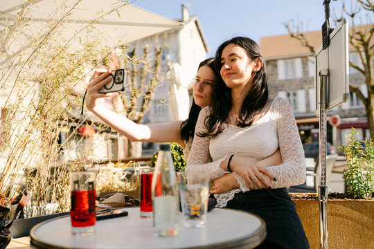 two friends hanging out in outdoor caf&eacute;, taking a seflie
