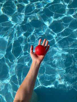hand holding red plastic ball in swimming pool in sunny day