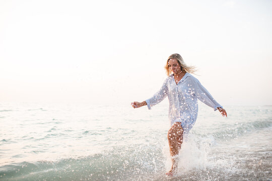 Young adult woman 30-35 year old having fun running in water splashes at beach over sea at background. Summer vacation time. Happiness. Selective focus.