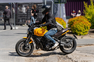 Fototapeta premium Modern individual urban transportation concept showing a person on a yellow naked motorcycle riding near sidewalk fences, active motorcycle rider street journey travel
