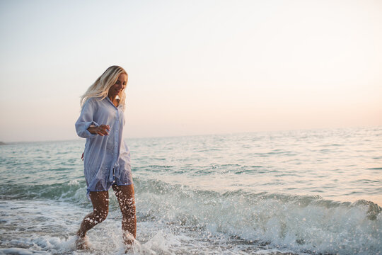 Young adult woman 30-35 year old having fun running in water splashes at beach over sea at background. Summer vacation time. Happiness. Selective focus.
