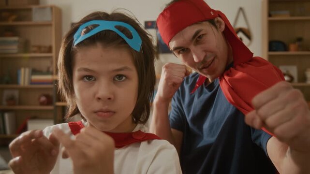 Portrait of father and child wearing superhero capes, posing playfully with fists raised at camera. Footage ideal for Fathers Day promotions, family bonding concepts, or creative play ads