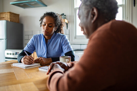 Home healthcare nurse consulting senior at kitchen table