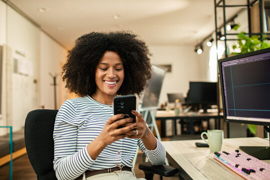 Smiling woman using smartphone at desk in modern office