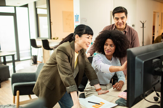 Coworkers collaborating at desktop computer in modern office