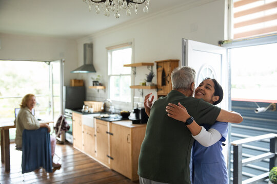 Home care nurse hugging senior man at kitchen doorway