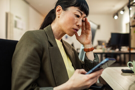 Concerned businesswoman checking smartphone at office desk