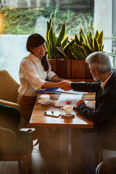 Smiling business colleagues shaking hands in coffee shop
