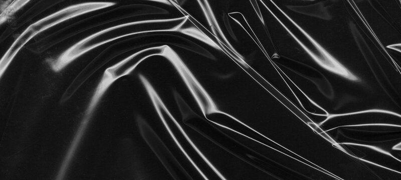 Close up view of smooth black plastic sheet with subtle graceful curves and soft highlights reflecting ambient light across glossy surface providing elegant moody atmosphere for digital compositing