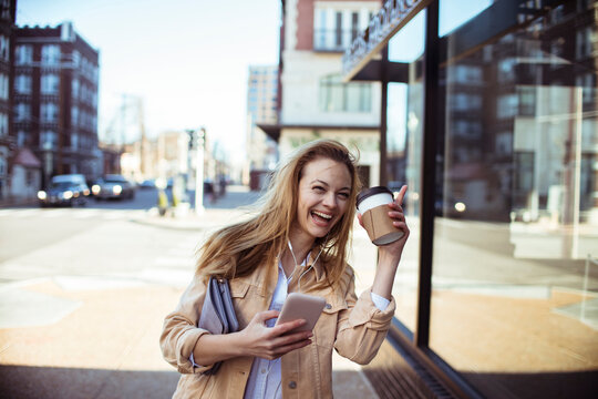 Smiling young woman with coffee and phone on city street