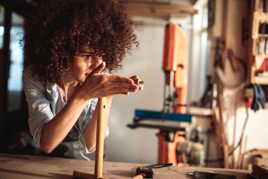 Focused craftswoman measuring dowel in woodworking workshop
