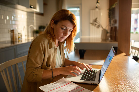 Focused woman managing finances on laptop at home kitchen table