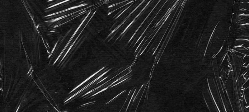 Stretched black plastic wrap texture with multiple parallel creases and intense light reflections providing high quality overlay for packaging design concepts and dark background visual aesthetics