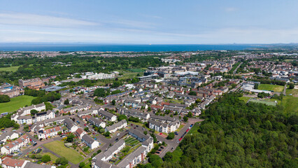 Fototapeta premium Beautiful aerial panorama of the Greendykes residential neighborhood in Edinburgh, Scotland. Scenic suburban cityscape with houses and green trees stretching to the sea coast on a sunny summer day.