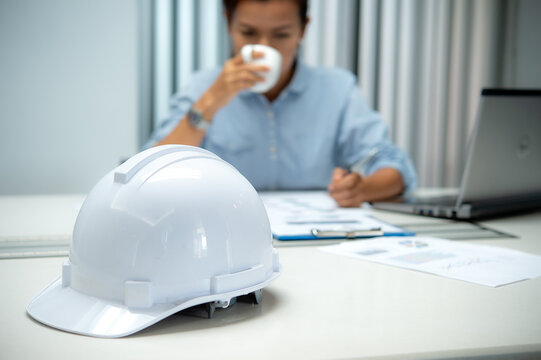 White safety helmet on desk with female engineer working in office construction concept