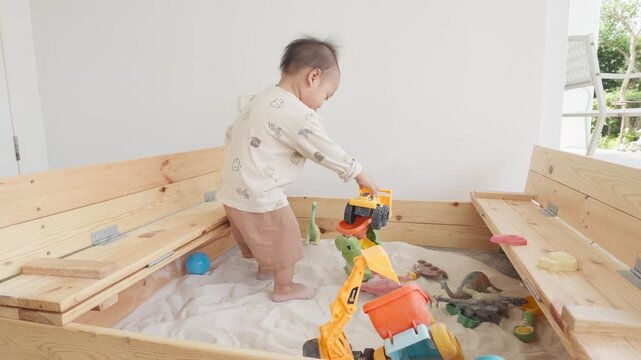 A young child enjoys playing in a sandbox filled with bright toys, fostering creativity and sensory exploration in a safe environment.