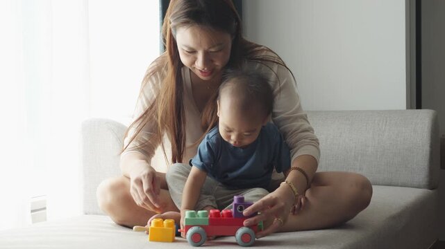 A heartwarming scene of a mother and her child engaging in playtime with a colorful toy on a sofa. The interaction highlights the bond between parent and child in a cozy indoor setting, fostering crea