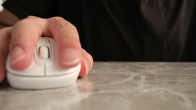 Close up of a hand clicking a white computer mouse and using the scroll wheel on a marble office desk