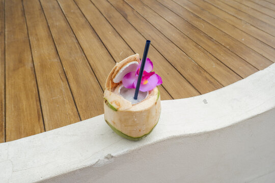 Tropical fresh coconut cocktail decorated with flowers and sandy beach by the sea,tropical resort villa,island summer travel,ocean backdrop,hotel for holiday vacation concept.