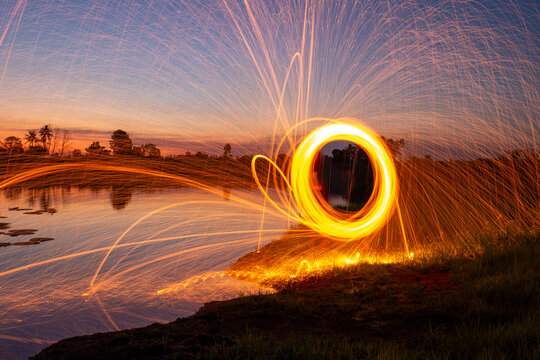 Spectacular steel wool spinning creating bright flying sparks over a calm lake during a golden sunset.