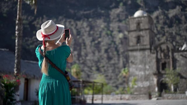 A senior woman smiles as she captures photos in front of San Javier Mission in Baja California Sur at sunrise, enjoying her adventure