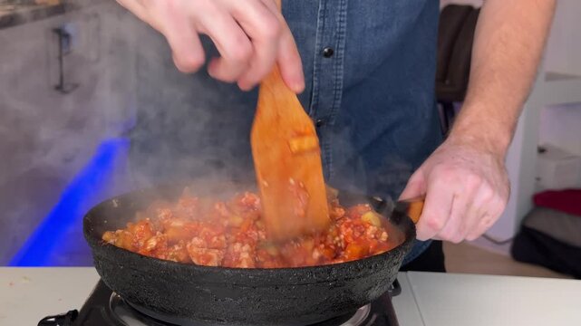 Hands stirring steaming tomato sauce in cast-iron skillet on stovetop