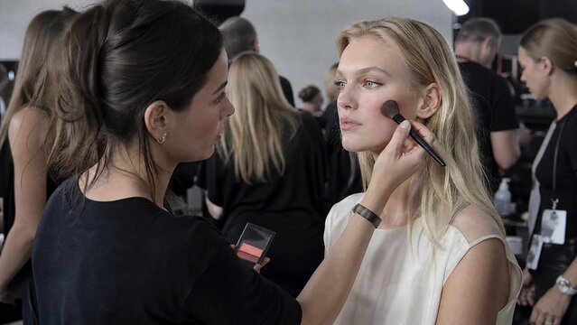 Professional Makeup Artist Applying Blush to a Beautiful Blonde Model Backstage