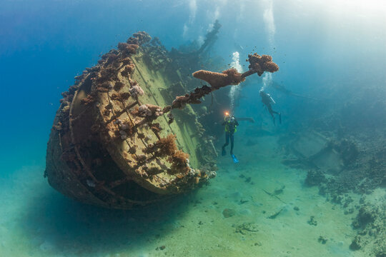 Cinematic underwater view of deep sea scuba diving excursion around an old coral overgrown ship wreck in clear blue ocean water.