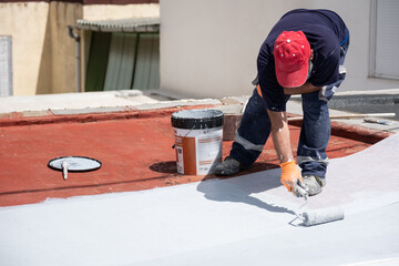 Worker applying white waterproofing liquid membrane on a red roof with a paint roller © Ladanifer
