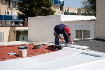 Construction worker applying a white waterproof membrane on a red flat roof during renovation © Ladanifer