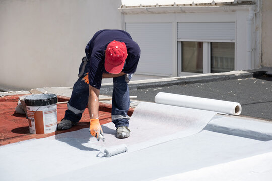 Worker applying a protective membrane on a flat building roof for renovation and insulation