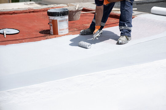 Worker applying white liquid membrane coating a roof surface for waterproofing