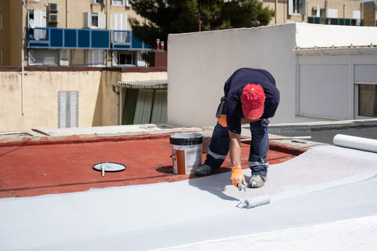 Worker applying white liquid membrane to a red roof surface using a roller