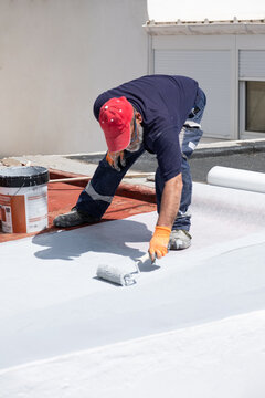 Building contractor applying white waterproofing liquid membrane to a flat roof