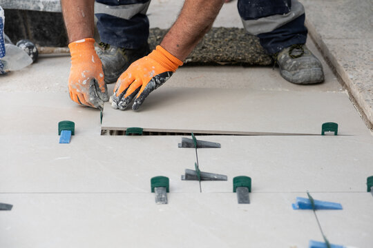 Tiler hands installing ceramic floor tiles using wedges and clips for even surface