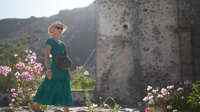 A senior woman walks and smiles in the garden of San Javier Mission as the sun rises in Baja California Sur, near Loreto