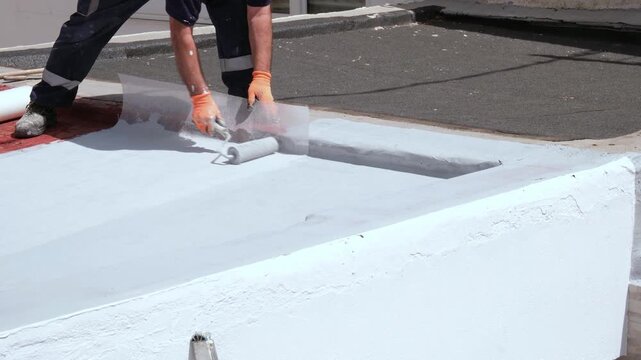 Roofer applying a waterproofing membrane and resin with a roller on a building's flat roof