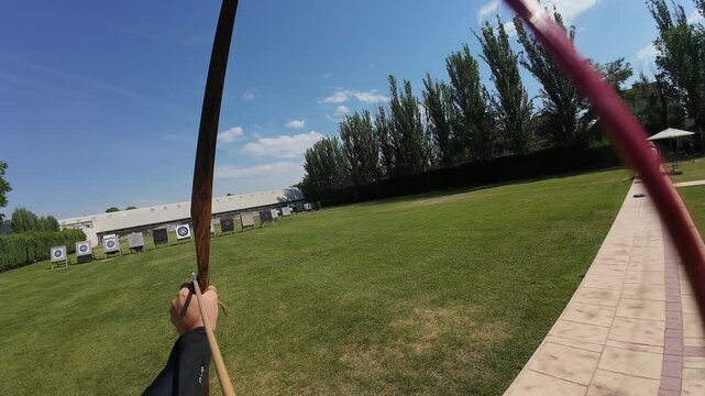 Archer aiming a traditional wooden bow at targets on a green field