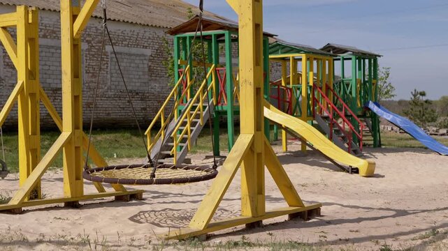 A colorful outdoor children playground features a yellow nest swing and various slides over a sand pit under a bright blue sky. Concept of childhood leisure and safe play areas for kids.