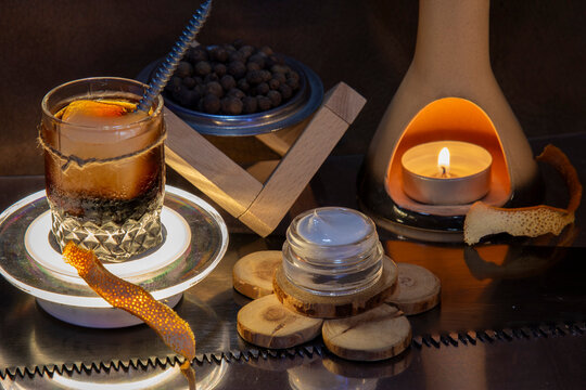 Men's wellness and grooming mockup. Blank open cosmetic jar for beard wax or pomade next to a dark cocktail and lit candle. Rustic industrial presentation with copy space.