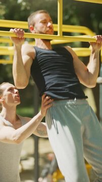 A man performs pull-ups with the help and motivation of his training partner at an outdoor gym. They celebrate their fitness achievement with a high-five