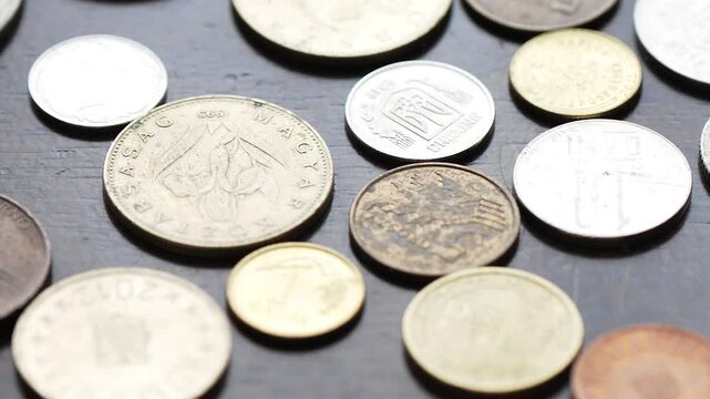 A variety of world coins scattered on a dark wooden table texture
