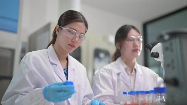 Scientists in lab coats and safety glasses conduct experiments with test tubes and microscopes