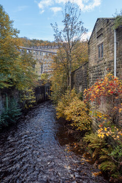 Autumn scene with Hebden water running though Hebden Bridge surrounded by trees and traditional stone houses