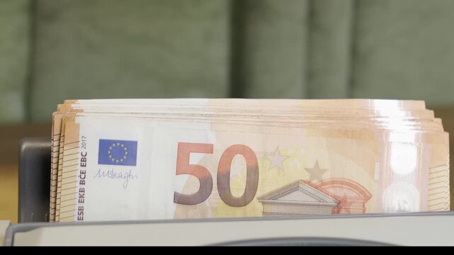 Close up of an automatic cash counter machine fast counting a stack of fifty euro paper bills. Financial, commercial, and banking concept, currency exchange, cash management, or inflation in Europe.