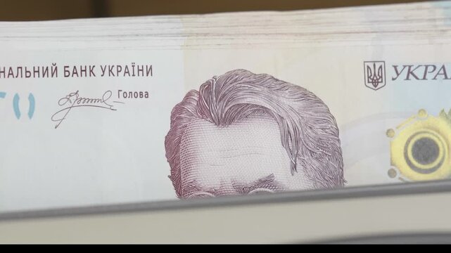 Close up shot of an automatic banknote counter machine fast processing a stack of 1000 Ukrainian hryvnia paper bills. Financial concept of banking operations, cash management, currency details, and